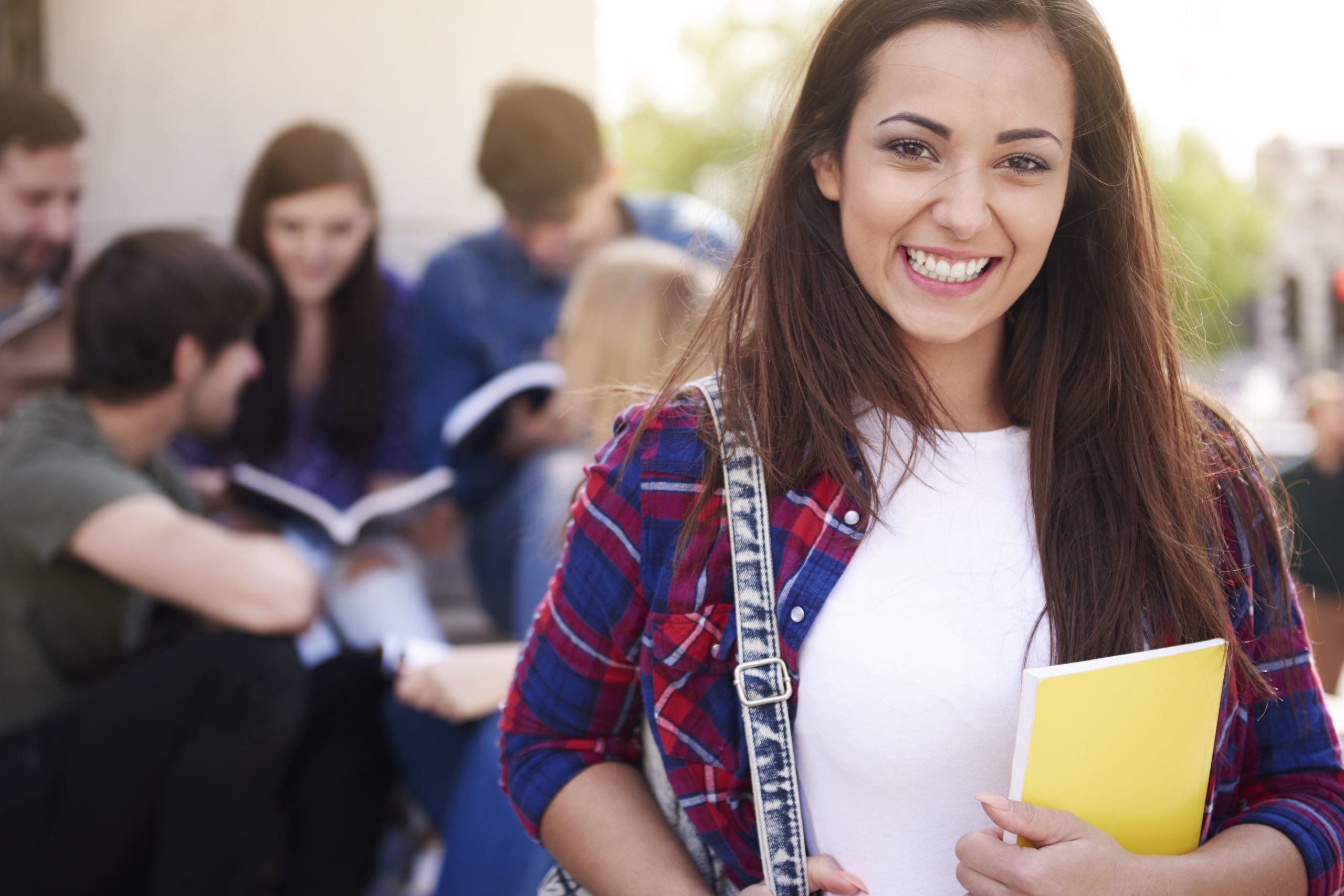 Aluna adolescente sorridente segurando livros com colegas ao fundo