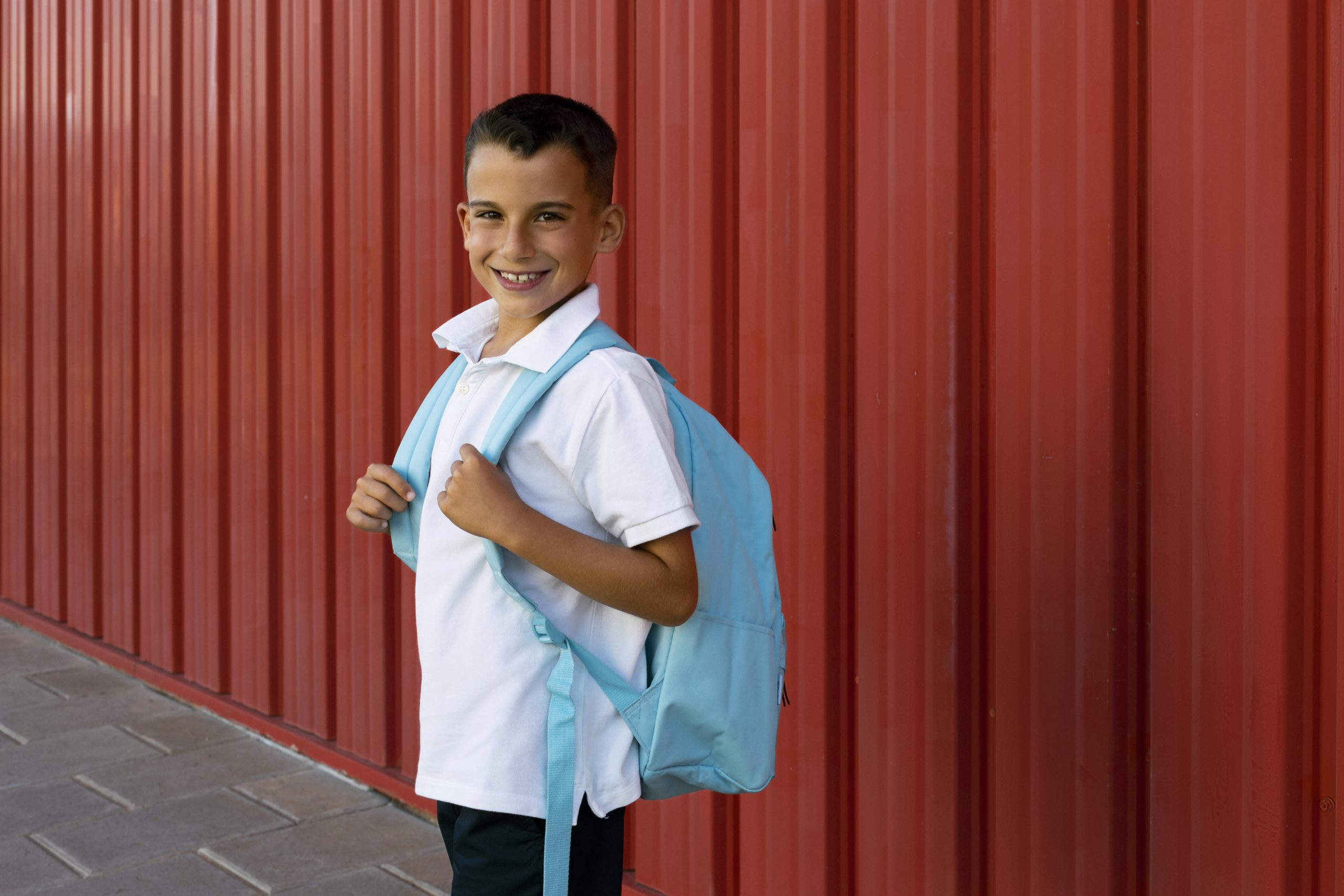 Menino sorridente posa carregando sua mochila nas costas
