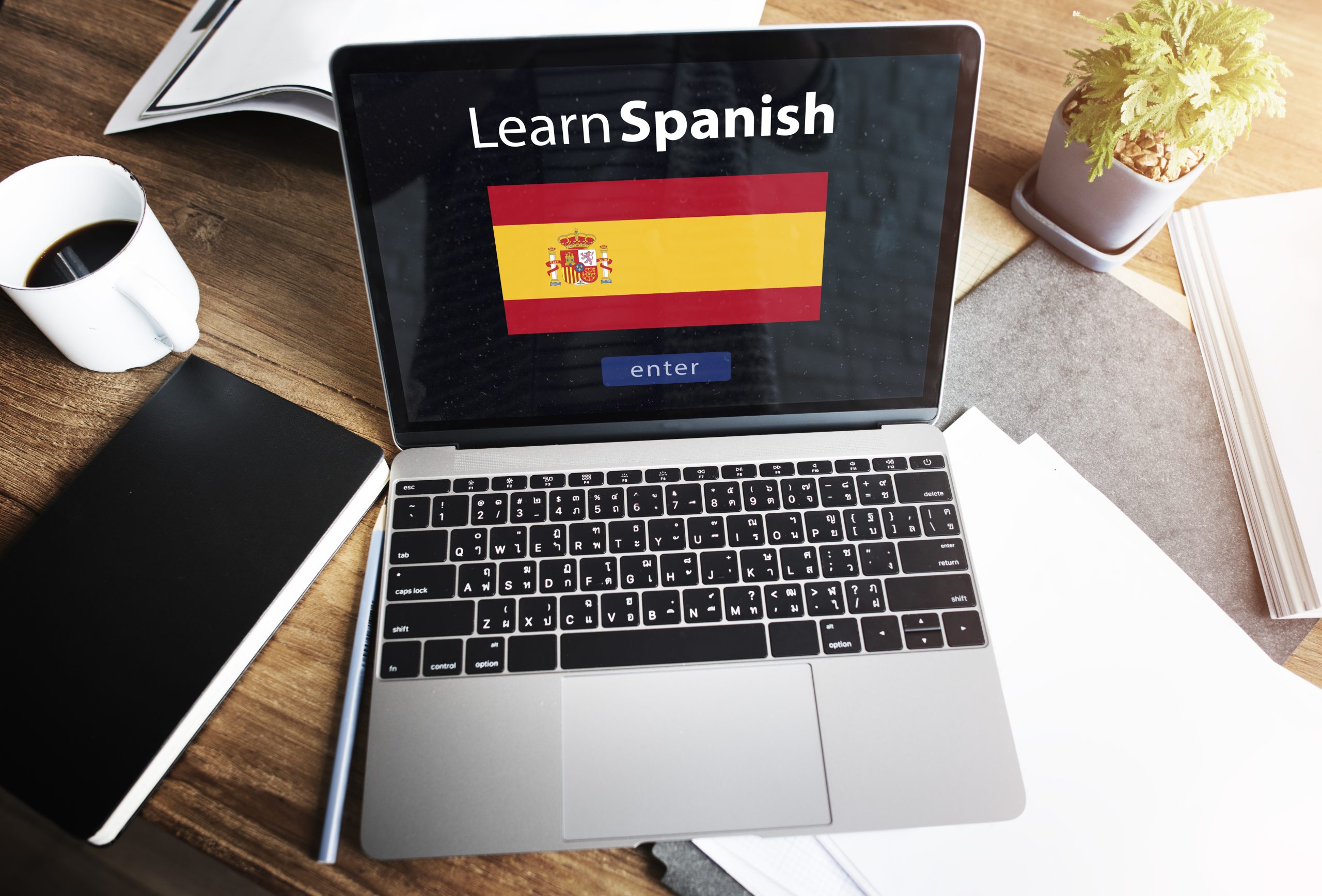 Notebook aberto em cima de uma mesa com uma bandeira da Espanha escrito acima aprender espanhol