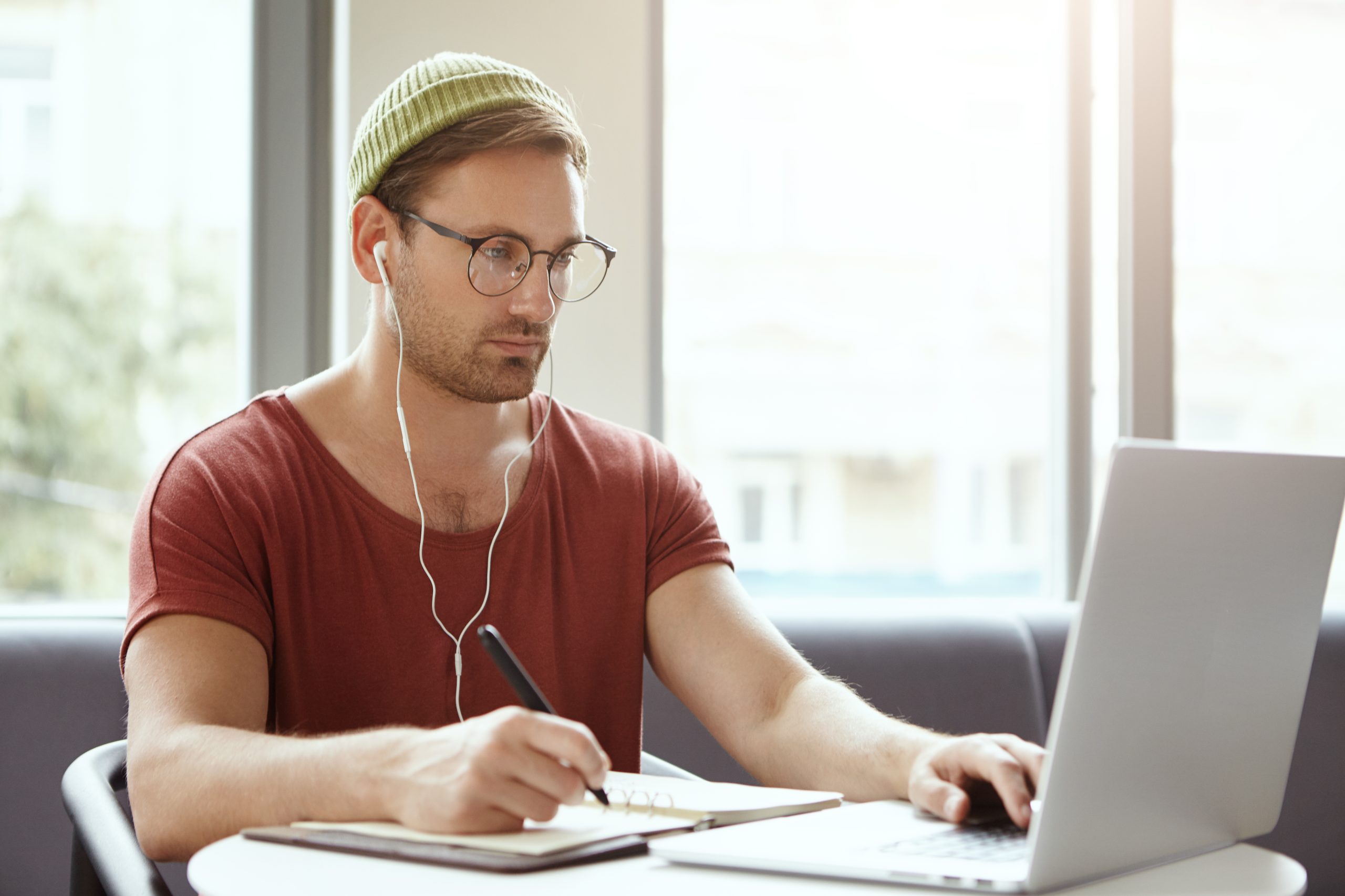 homem estuda anotando em um caderno diante um notebook aberto