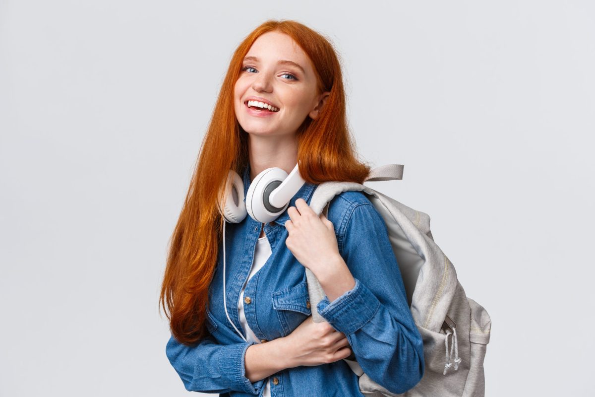 Jovem estudante sorridente posa de lado com uma mochila no ombro