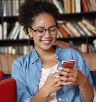 Uma aluna está na biblioteca e olha atentamente para o celular, onde confere o Boletim Online 2024 RS