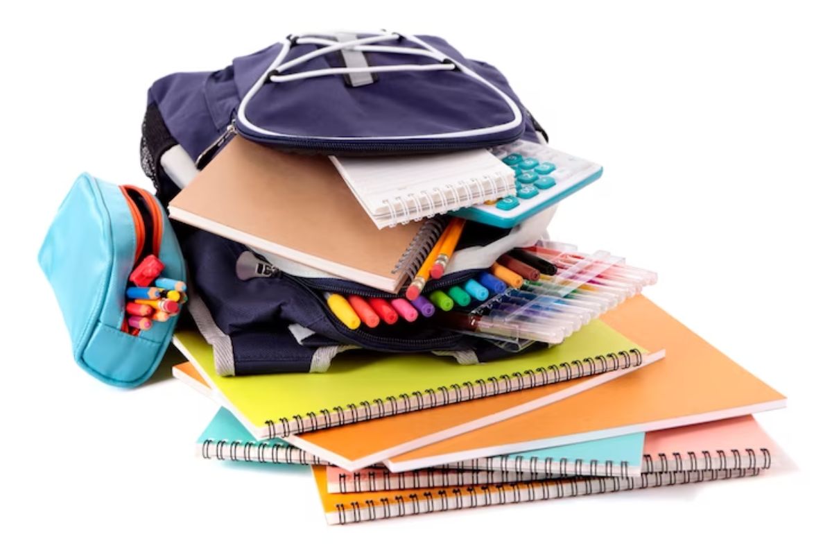 Alguns materiais escolares em cima de um fundo branco. Há mochila, canetinhas, e cadernos